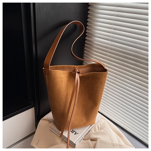 Detail of a brown suede bucket bag featuring drawstring closure and retro chic texture