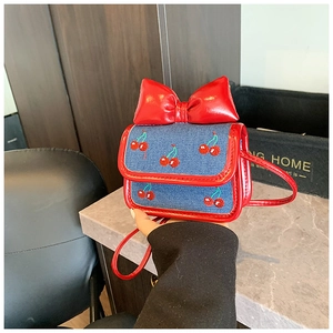 Detail of mini blue denim crossbody bag featuring cherry embroidery and red bow accent