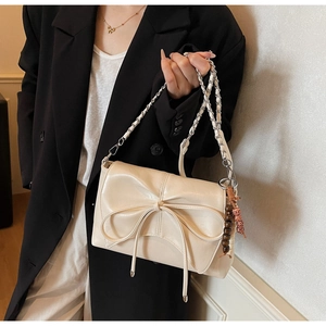Detail of cream PU leather shoulder bag featuring a large bow and metallic chain strap