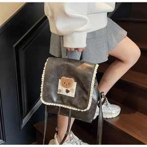 Close-up of vintage dark gray leather backpack with white lace edges and plush bear patch