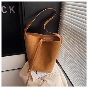 Detailed view of brown suede bucket bag with decorative tie on a minimalist background