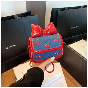 Detail of denim mini bag with cherry embroidery and shiny red leather bow
