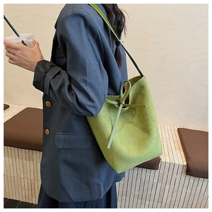 Detail of green suede bucket bag featuring a decorative bow knot and shoulder strap