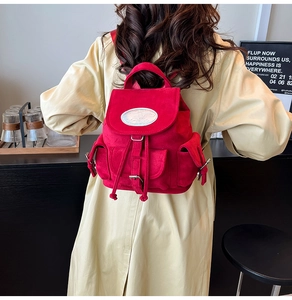 Gros plan d'un sac à dos en velours rouge porté avec un trench beige au style élégant