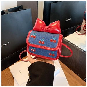 Detail of blue denim mini bag with cherry embroidery and large red glossy bow decor