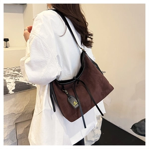 Detail of dark brown suede tote bag with fringe and logo tag on a female model