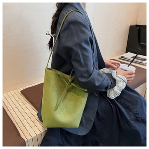Detailed close-up of avocado green suede bucket bag with decorative tie on a wooden bench
