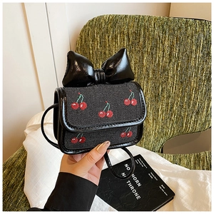 Close-up of black mini crossbody bag with a large bow and red cherry embroidery