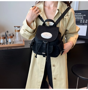 Détail du mini sac à dos noir avec fermeture à cordon et écusson ovale coloré sur rabat
