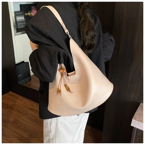 Beige leather hobo shoulder bag with wooden bead tassel shown on model's shoulder