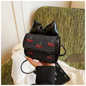 Close-up of a mini crossbody bag with a large black bow and cherry embroidery detail