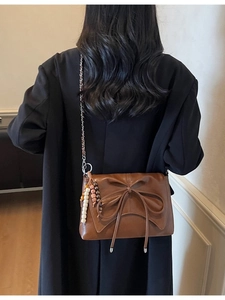 Dark brown leather shoulder bag with a large bow and colorful beaded charm on a model