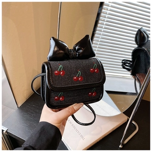 Detail of a mini black crossbody bag featuring red cherry embroidery and a large bow