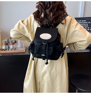 Détail d'un sac à dos en daim noir avec rabat à cordon et plaque métallique ovale