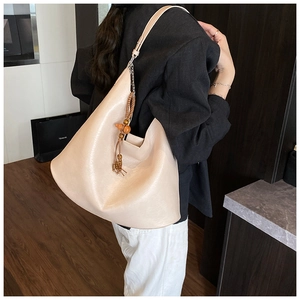 Detail of beige faux leather crescent bag featuring a wood bead and tassel decorative charm