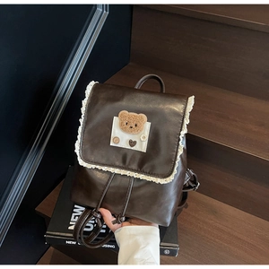 Detail of dark brown vintage backpack with lace trim and plush bear patch on front flap