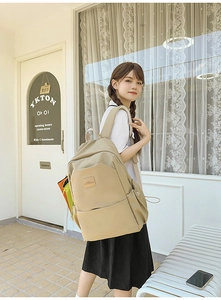 Model wearing a large beige laptop backpack with side pockets in a stylish cafe setting