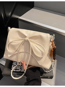 Cream women shoulder bag with bow decor, chain strap on urban stairs background