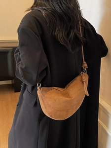 Brown suede crescent moon bag with knot detail shown on a model in a black coat