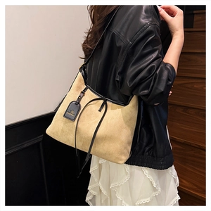 Close-up of khaki suede tote bag with black leather trim and decorative tassel details