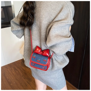 Detail view of denim crossbody bag with red leather bow and cherry embroidery accents