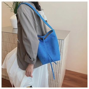 Close-up of bright blue suede bucket bag showing soft texture and decorative drawstring