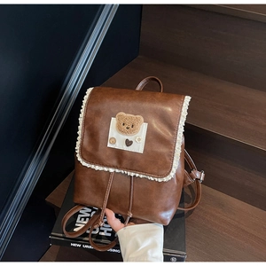Detail of vintage brown backpack with white lace trim and cute plush bear patch