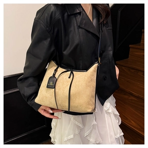 Detail of a large beige suede tote bag with black leather trim worn on a model