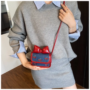 Detail of mini denim crossbody bag featuring cherry embroidery and a large red bow accent