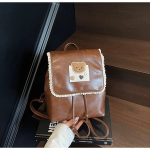 Detail of vintage brown leather backpack featuring delicate lace trim and plush bear patch