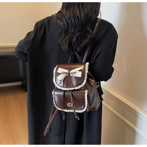 Detail of a dark brown mini leather backpack with lace trim and bow on a model