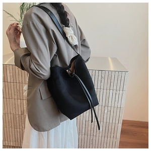 Detail of a minimalist black suede bucket bag styled with a gray blazer and long skirt