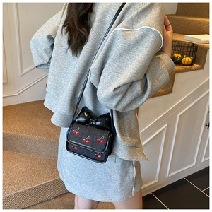 Detailed close-up of a mini crossbody bag with cherry embroidery and a large black bow