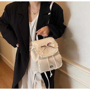 Close-up of cream backpack with lace trim and brown striped bow detail on flap