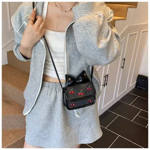 Mini black crossbody bag with red cherry embroidery and oversized bow detail on a grey outfit