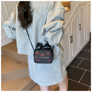 Detail of a black mini crossbody bag with cherry embroidery and a large bow on the strap