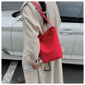 Detail of red suede bucket bag with elegant bow tie decoration and long shoulder strap