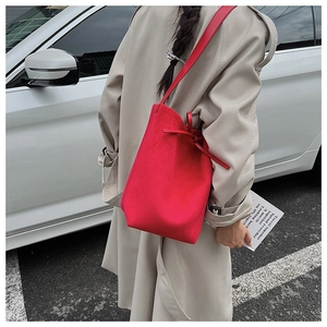 Close-up of red suede bucket bag with drawstring bow detail on beige trench coat