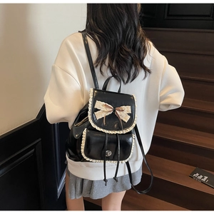 Detail of black faux leather backpack with cream lace trim and bow on a model