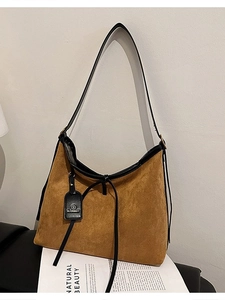 Brown faux suede tote bag with black leather trim and tassels shown on a minimalist table