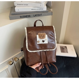 Close-up of brown faux leather backpack with white lace trim and cute teddy bear patch