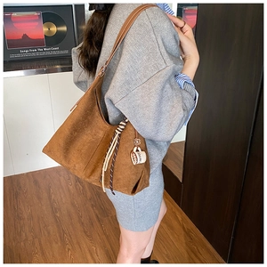 Détail d'un sac hobo en daim marron avec un pendentif café et une bandoulière en cuir