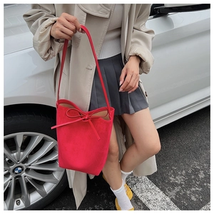 Macro detail of red suede bucket bag with drawstring bow and slim shoulder strap