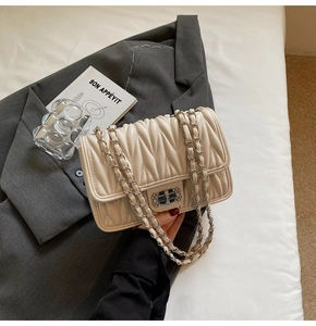 Detail einer cremefarbenen Stepptasche mit Strass-Schnalle auf grauem Blazer