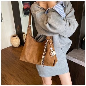 Détail d'un grand sac hobo en daim marron avec breloque tasse à café et gland à rayures