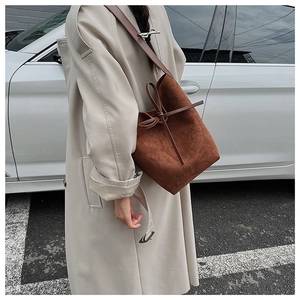 Brown suede bucket bag with bow drawstring shown on model wearing a beige trench coat