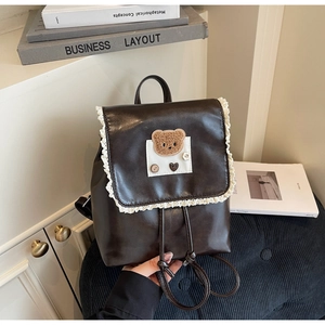 Detail of dark brown leather backpack with lace trim and plush bear patch decoration