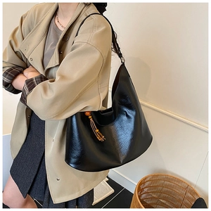 Detail of black soft leather shoulder bag with vintage orange bead and tassel charm