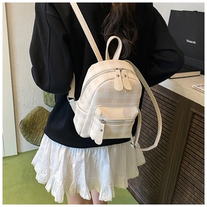 Dettaglio di uno zaino a scacchi color crema indossato per un look da viaggio casual