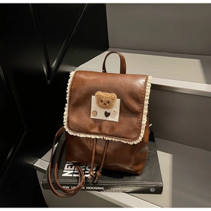 Detail of a brown leather backpack with lace trim and a cute plush bear ornament
